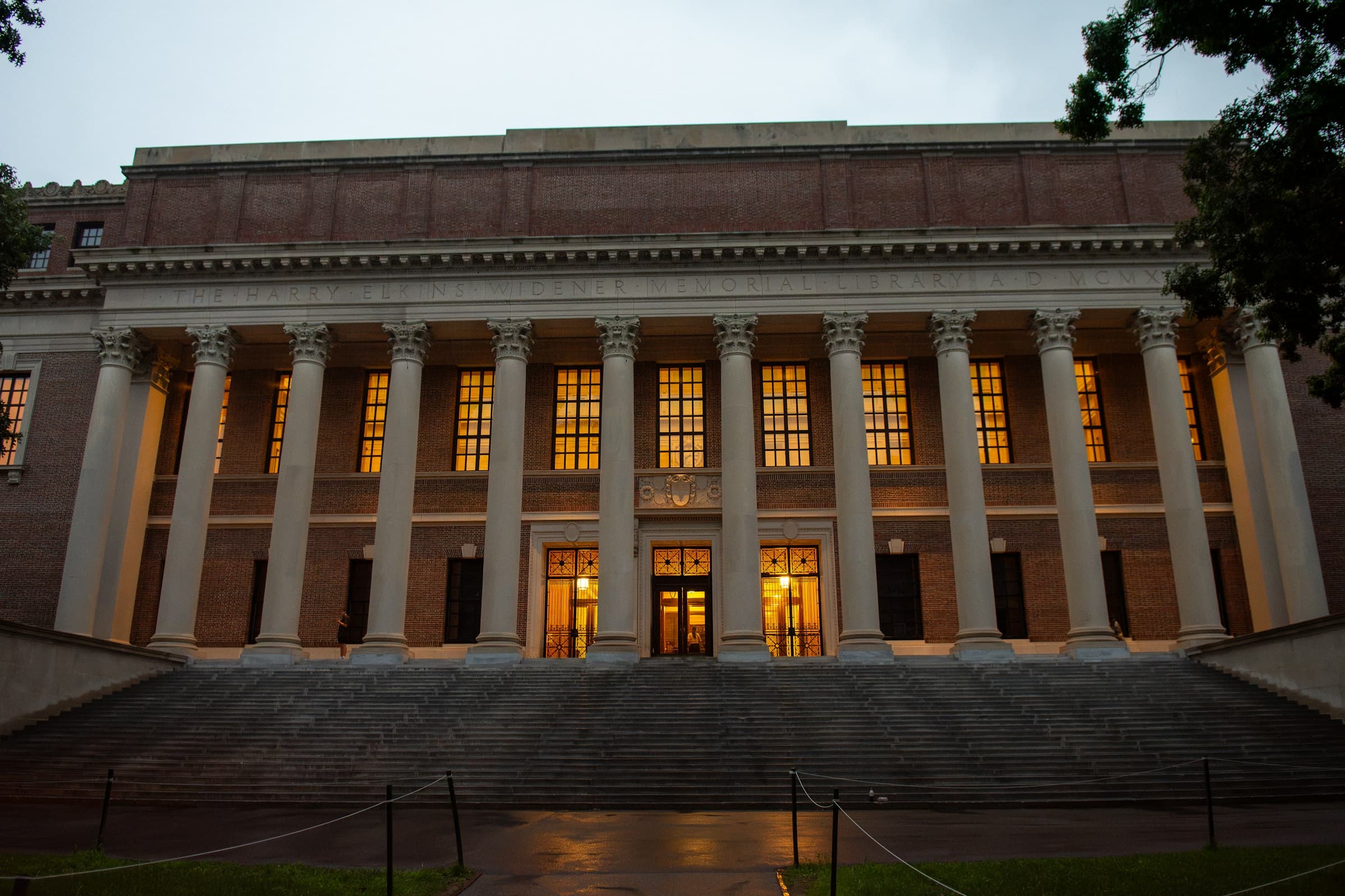 Columned university library with its windows lit at dusk