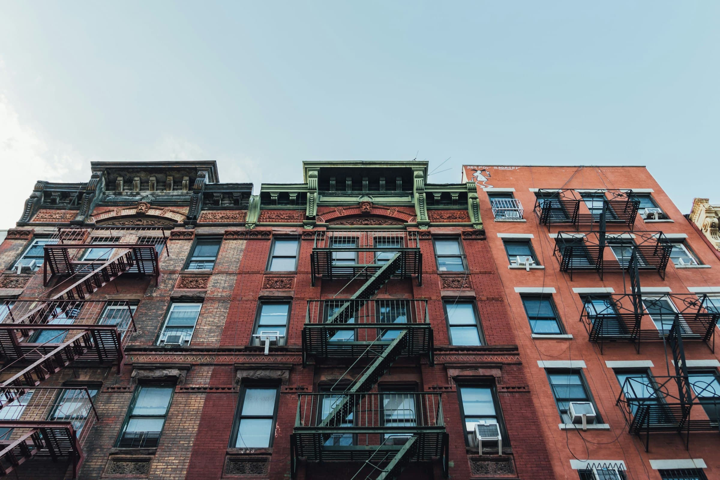 Red-brick apartment buildings with iron fire escapes, seen from the street