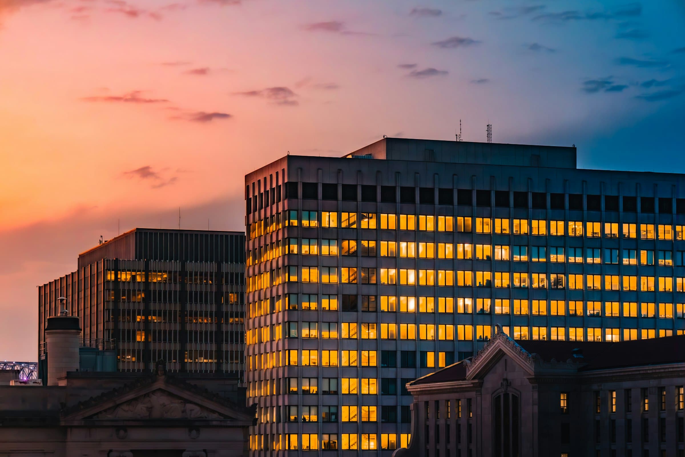 Office building windows glowing gold against a pink dusk sky